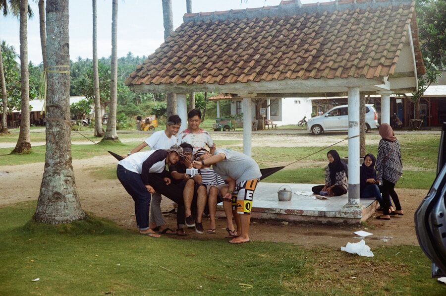 Group sitting outdoors under a shelter, sharing phone.
