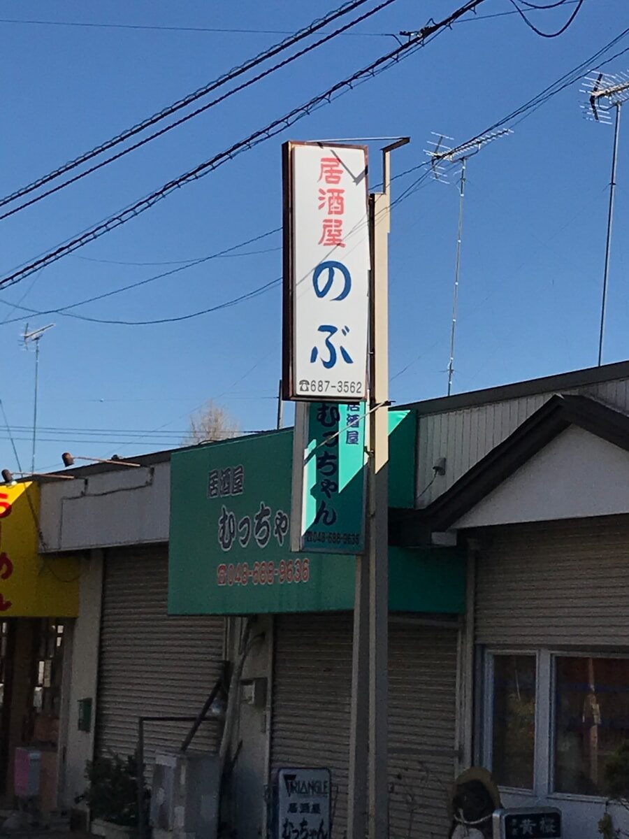 Japanese izakaya street sign under blue sky.